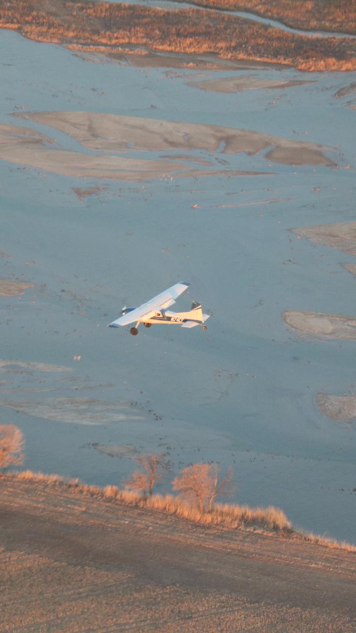 Small aircraft flying above braided river channels during early morning light.