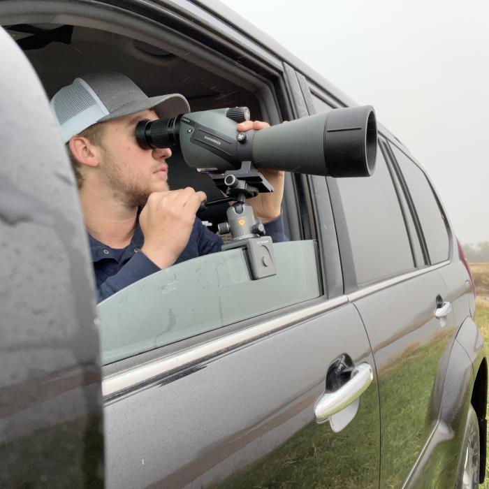 Researcher looking through a spotting scope mounted in a vehicle window.